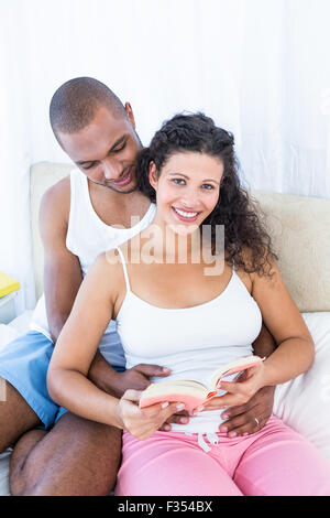 Portrait de femme enceinte holding book avec mari on bed Banque D'Images