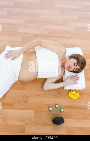 Femme enceinte avec les yeux fermés allongé sur plancher de bois franc Banque D'Images