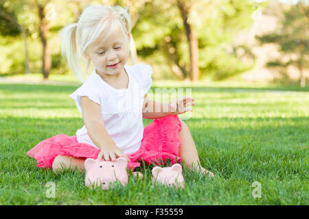 Cute Little Girl s'amusant avec ses grandes et petites tirelires dehors sur l'herbe. Banque D'Images