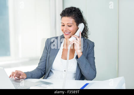 Pregnant businesswoman talking on phone while working on laptop Banque D'Images