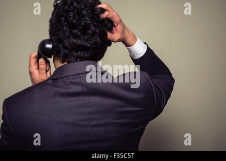 Vue arrière d'un homme confus sur le téléphone se gratte la tête Banque D'Images