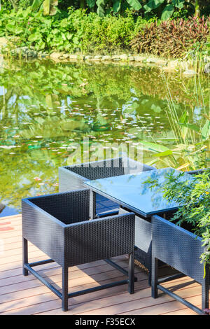 Espace de détente avec table et fauteuils en rotin au bord d'une piscine dans le jardin Banque D'Images