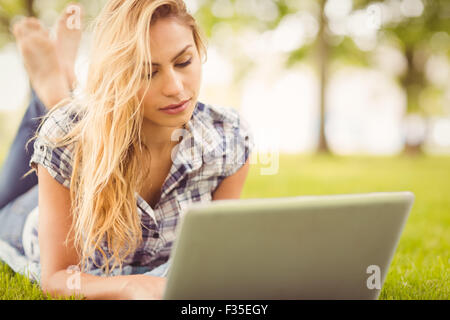 Woman using laptop while lying on grass en avant Banque D'Images