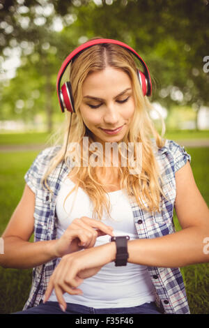 Smiling woman listening to music et à l'aide tandis que smartwatch sitting on grass Banque D'Images
