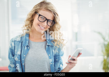 Portrait of smiling woman wearing eyeglasses tandis que holding smartphone Banque D'Images