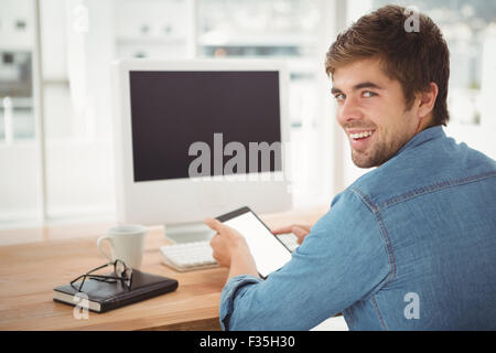 Happy businessman using digital tablet while sitting at desk Banque D'Images