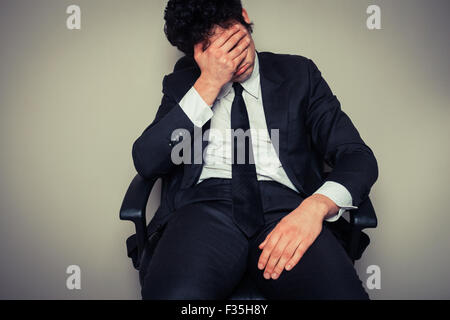 Triste et fatigué young businessman sitting dans une chaise de bureau Banque D'Images