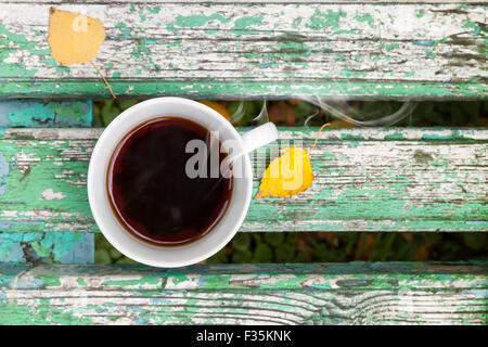 Tasse de thé noir blanc est sur le vieux banc en bois vert en automne parc. Focus sélectif avec DOF peu profondes Banque D'Images