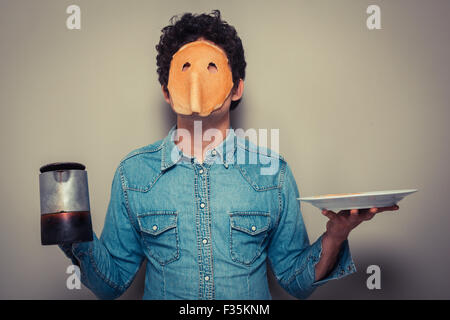 Jeune homme a coupé en orbites une crêpe et porte sur son visage tout en maintenant un pot de café Banque D'Images