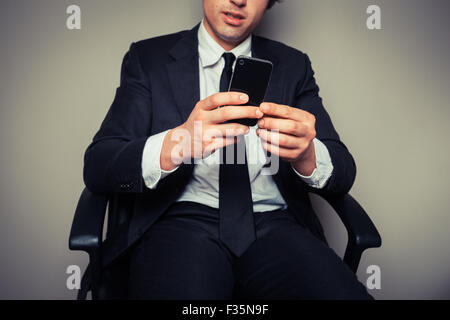 Jeune homme assis dans une chaise de bureau est à l'aide de son téléphone intelligent Banque D'Images