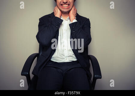 Un jeune homme assis dans une chaise de bureau est d'avoir des douleurs au cou Banque D'Images