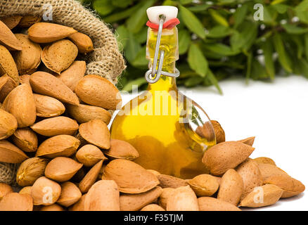 L'huile d'Amande bio frais dans une bouteille de verre swing top montrant les amandes cueillies dans un sac en toile de jute avec verdure dans le floue retour Banque D'Images