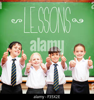 Leçons contre cute pupils showing Thumbs up in classroom Banque D'Images