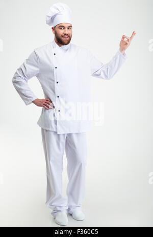 Full Length portrait of a happy chef cuisinier montrant le geste de bienvenue isolé sur fond blanc Banque D'Images