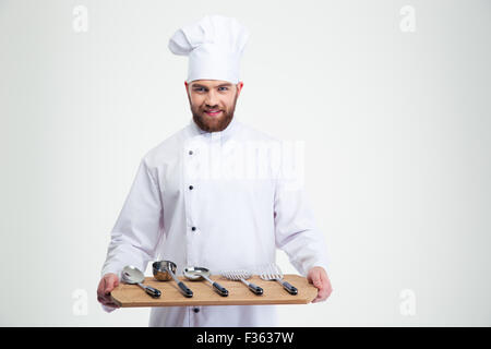 Portrait of a smiling male chef cook holding wooden chopping board avec cuillères isolé sur fond blanc Banque D'Images