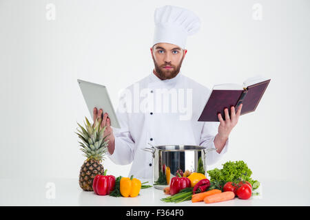 Portrait of a handsome male chef cuisinier table de réception ordinateur et livre de recettes alors que la préparation des aliments et looking at camera Banque D'Images