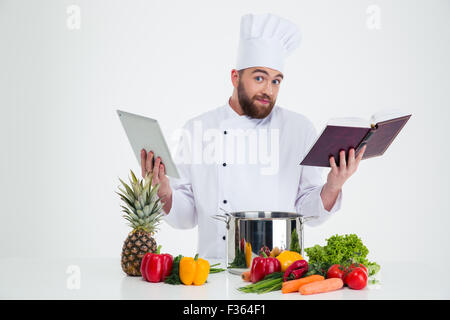 Portrait of a young male chef cook holding tablet computer et recette livre isolé sur fond blanc Banque D'Images