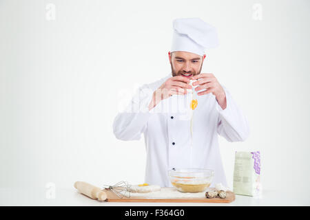 Portrait d'un homme heureux casser des œufs dans un bol pour la cuisson isolé sur fond blanc Banque D'Images