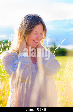 Un portrait en contre-jour d'une femme (âgés de 25 à 30) portant un haut blanc, se tenait dans un domaine de l'herbe longue sur un soir d'été Banque D'Images