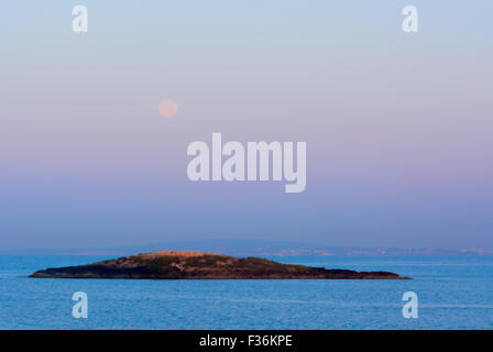 Réglage de la lune à l'aube en violet, bleu et rose lumière atmosphérique tout comme le soleil levant fait la lumière sur une petite île de la baie Banque D'Images