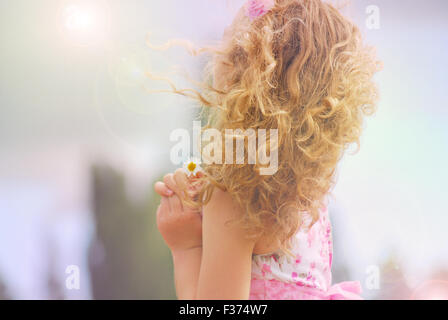 Jolie petite fille avec une fleur dans ses mains à la recherche le soleil et le ciel Banque D'Images