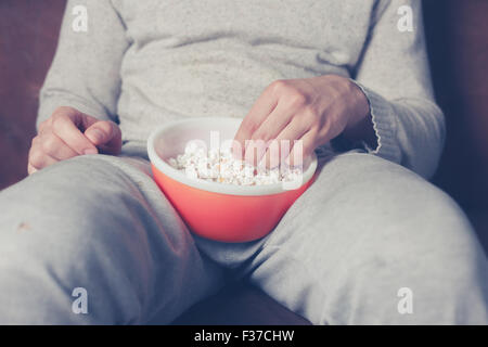 Jeune homme assis sur un canapé et eating popcorn Banque D'Images