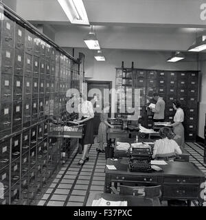 Historique, années 1950, personnel féminin travaillant dans une grande pièce remplie de hauts plafonds en métal brillant classeurs, plusieurs bureaux et machines à écrire. Banque D'Images