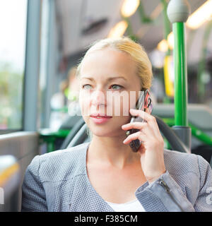 Blond caucasian business woman talking on cell phone, voyageant par autobus. Les transports publics et les déplacements quotidiens au travail. Banque D'Images