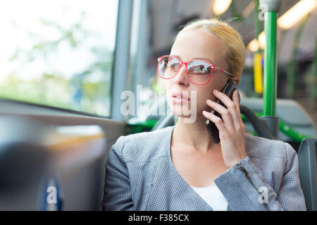 Blond caucasian business woman talking on cell phone, voyageant par autobus. Les transports publics et les déplacements quotidiens au travail. Banque D'Images