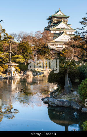 Principale du château d'Osaka vu de garder le parc du château d'Osaka. Heure d'or, tôt le matin, arbres en premier plan avec donjon derrière contre plae ciel bleu. Banque D'Images