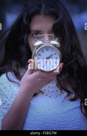Girl montrant un oeil seulement couvrant son visage d'une horloge dorée Banque D'Images