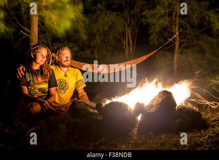 Feu de camp sur une plage rocheuse avec couple sitting Banque D'Images