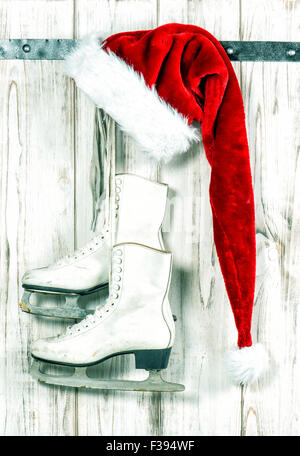 Décoration de Noël. Santas rouge hat et patins à glace blanc accroché sur fond de bois. Tons style vintage photo Banque D'Images