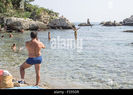 Un homme prenant photo de son ami dans la mer de l'île Isola Bella en Sicile. Banque D'Images