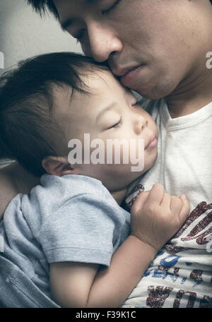 Portrait d'un homme avec ses yeux fermés tenant son fils endormi Banque D'Images