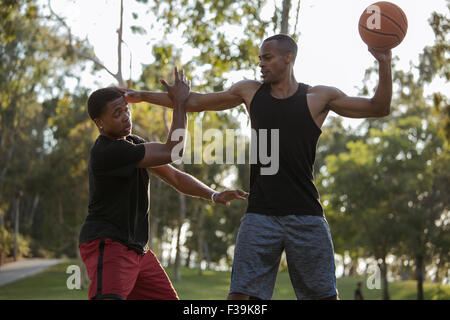 Basket-ball player retenant son adversaire dans le parc au coucher du soleil Banque D'Images