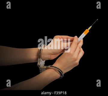 Les mains dans des menottes holding syringe isolé sur fond noir Banque D'Images