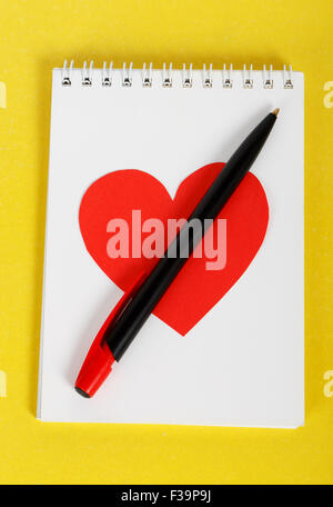 Coeur rouge avec un stylo noir sur blanc portable sur un fond jaune Banque D'Images