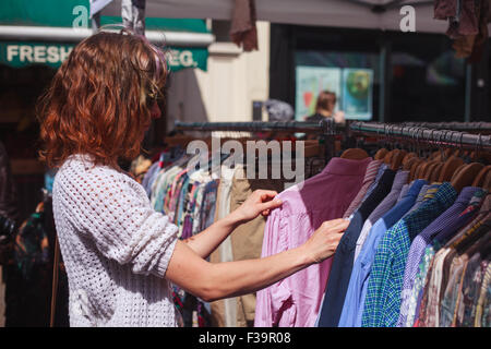 Une jeune femme consulte un rail de vêtements dans un marché de rue