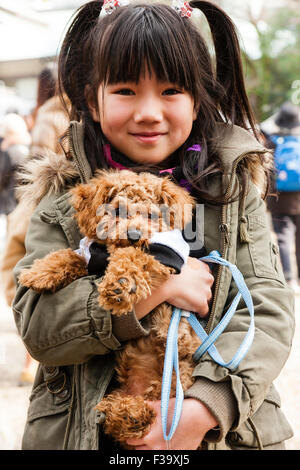 L'enfant japonais, fille, 9-10 ans, à enduire, souriant et posant pour viewer calins et pendant qu'elle détient dans les deux bras son chien de compagnie. Eye-contact. Banque D'Images