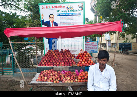 Vendre des pommes et des grenades l'homme en face d'un panneau commémorant B.R. Ambedkar, un célèbre homme politique indien chef. Banque D'Images