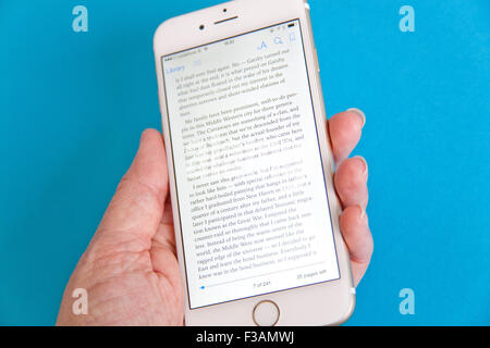 La lecture d'un ebook sur un or et blanc Apple iPhone 6 againdt un fond bleu Banque D'Images