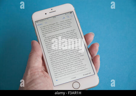 La lecture d'un ebook sur un or et blanc Apple iPhone 6 againdt un fond bleu Banque D'Images