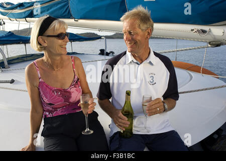 Vieux couple relaxing et souriant avec verre en soirée à bord d'un voilier Banque D'Images