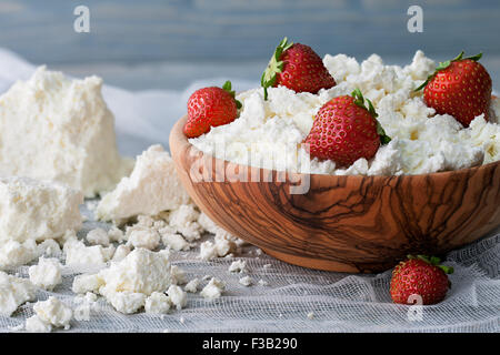 Un bol en bois avec du fromage cottage et de fraises fraîches sur un fond bleu Banque D'Images