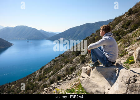 Un jeune homme assis sur la mer à la rock et belles contemplant la baie de Kotor au Monténégro Banque D'Images