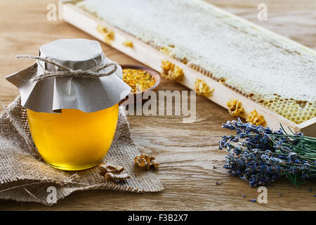 Pot en verre rempli de miel, un bouquet de lavande, d'abeilles et d'un bol en t avec du pollen d'abeille sur fond de bois. Banque D'Images