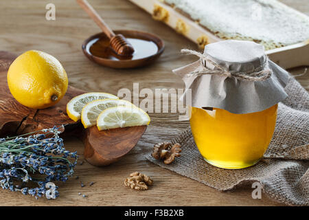 Un bocal en verre rempli de miel avec des morceaux de citron sur une planche à découper derrière. Banque D'Images