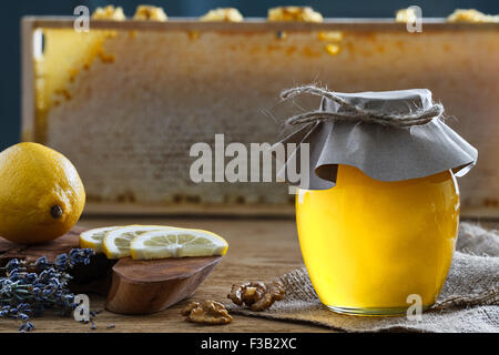 Un bocal en verre rempli de miel, avec un bouquet de lavande et de citron morceaux sur une planche à découper derrière. Banque D'Images