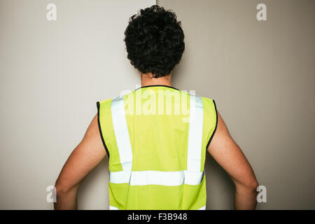 Vue arrière d'un constructeur dans un gilet contre un fond blanc et vert Banque D'Images